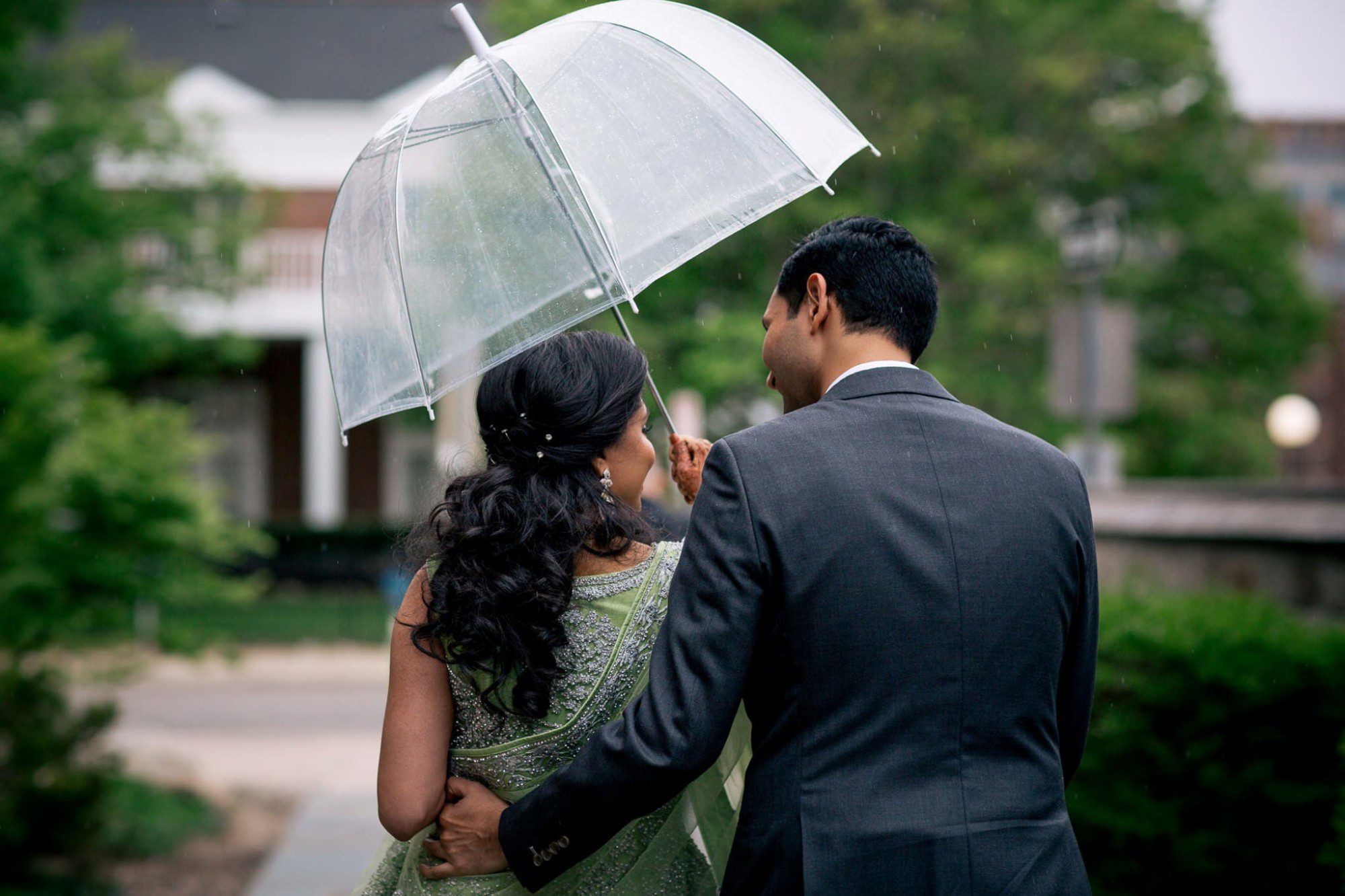 bride and groom walking in the rain under clear umbrella