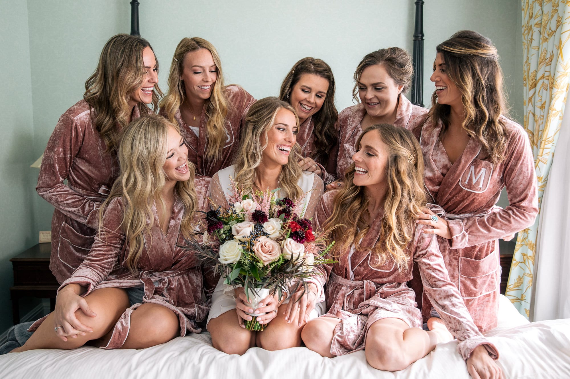 bride with bridesmaids laughing on top the bed