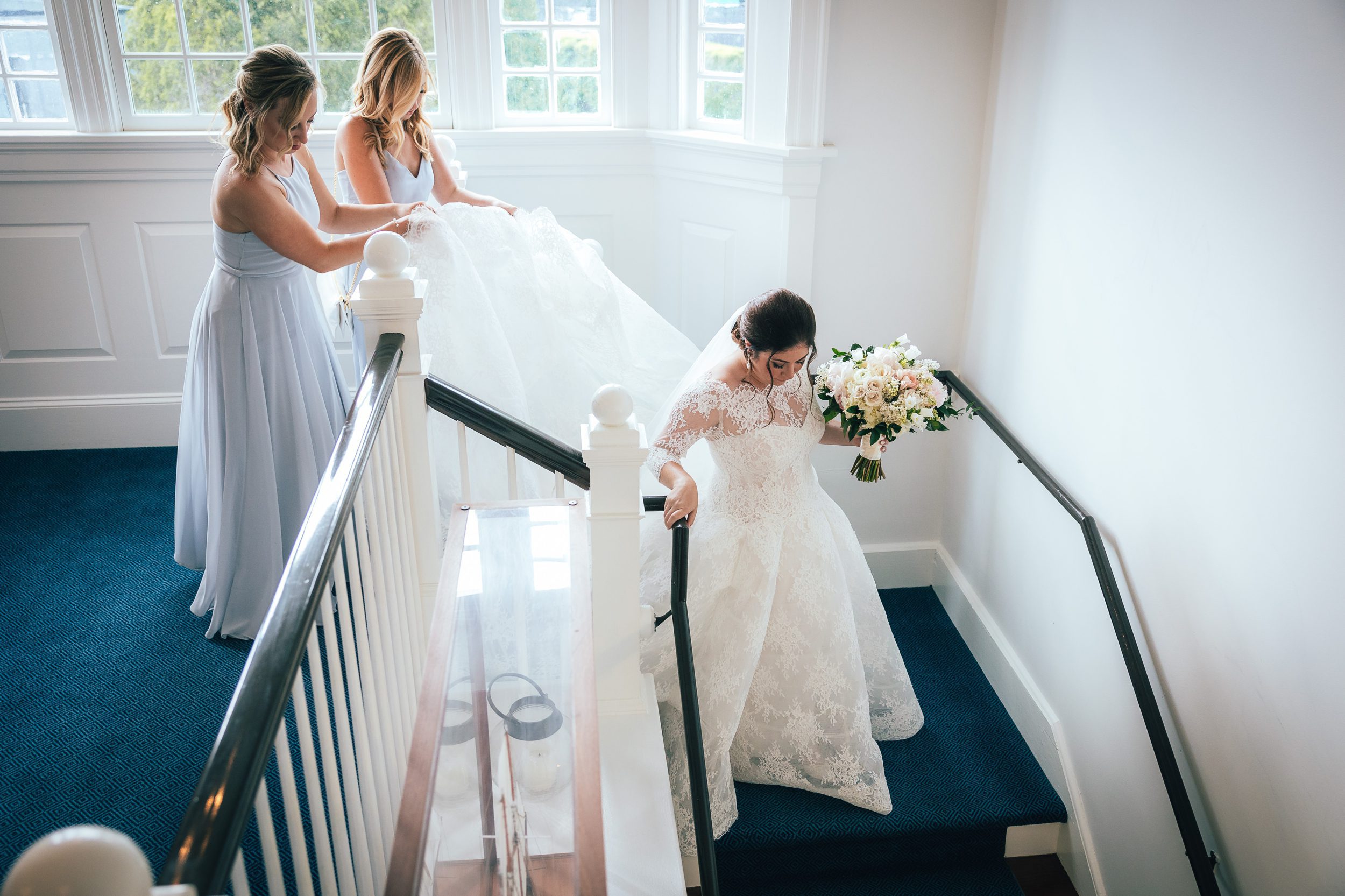 bridesmaids helping bride going down the stairs