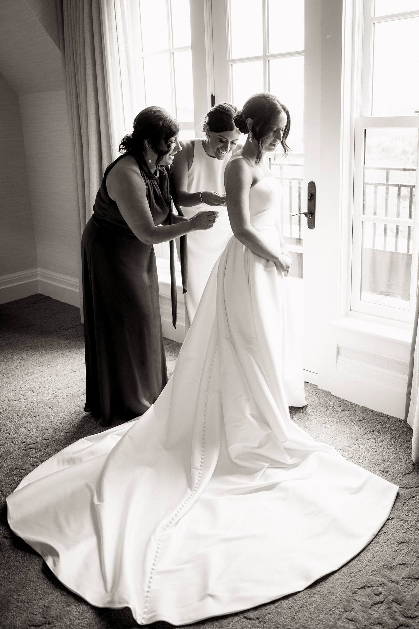mom and sister helping bride with wedding dress