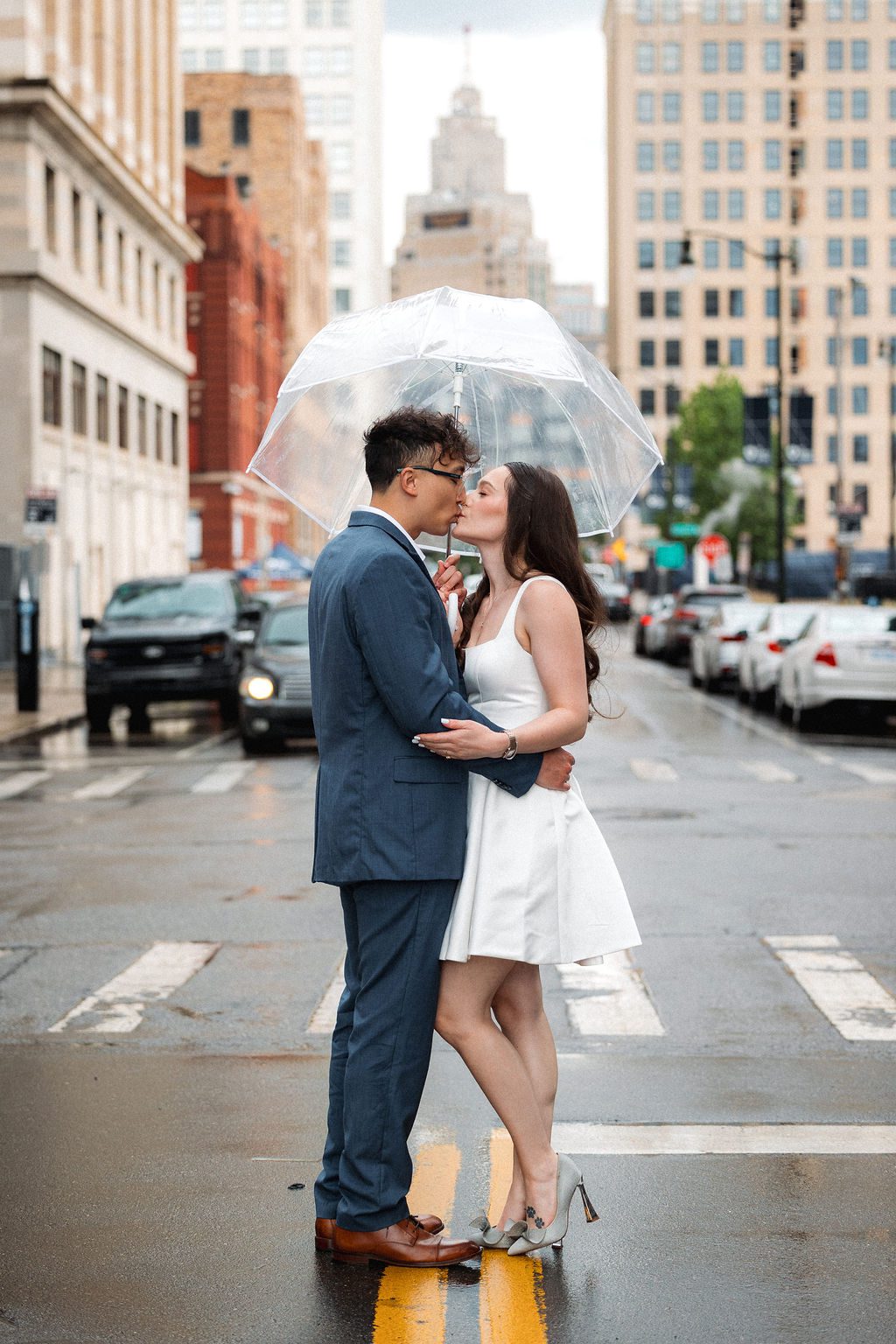 Couple Embrace in Rain Under Clear Umbrella During Photoshoot